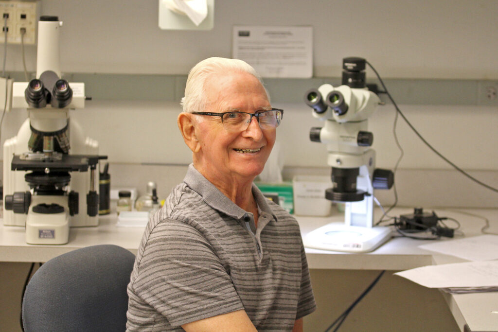 Photograph of Dr. Charles "Chuck" Hodges at his desk in front of microscopes